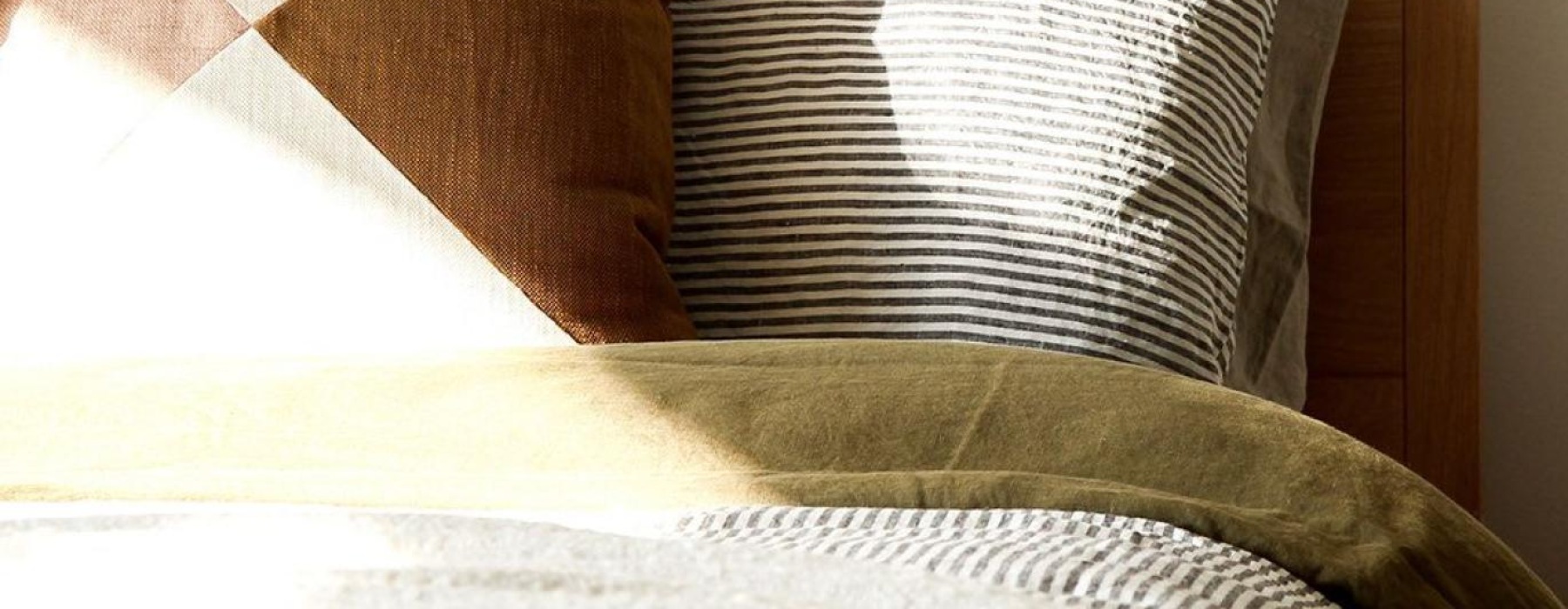 swath of sunlight shines across a well made bed and bedside table with a vase of cotton plants