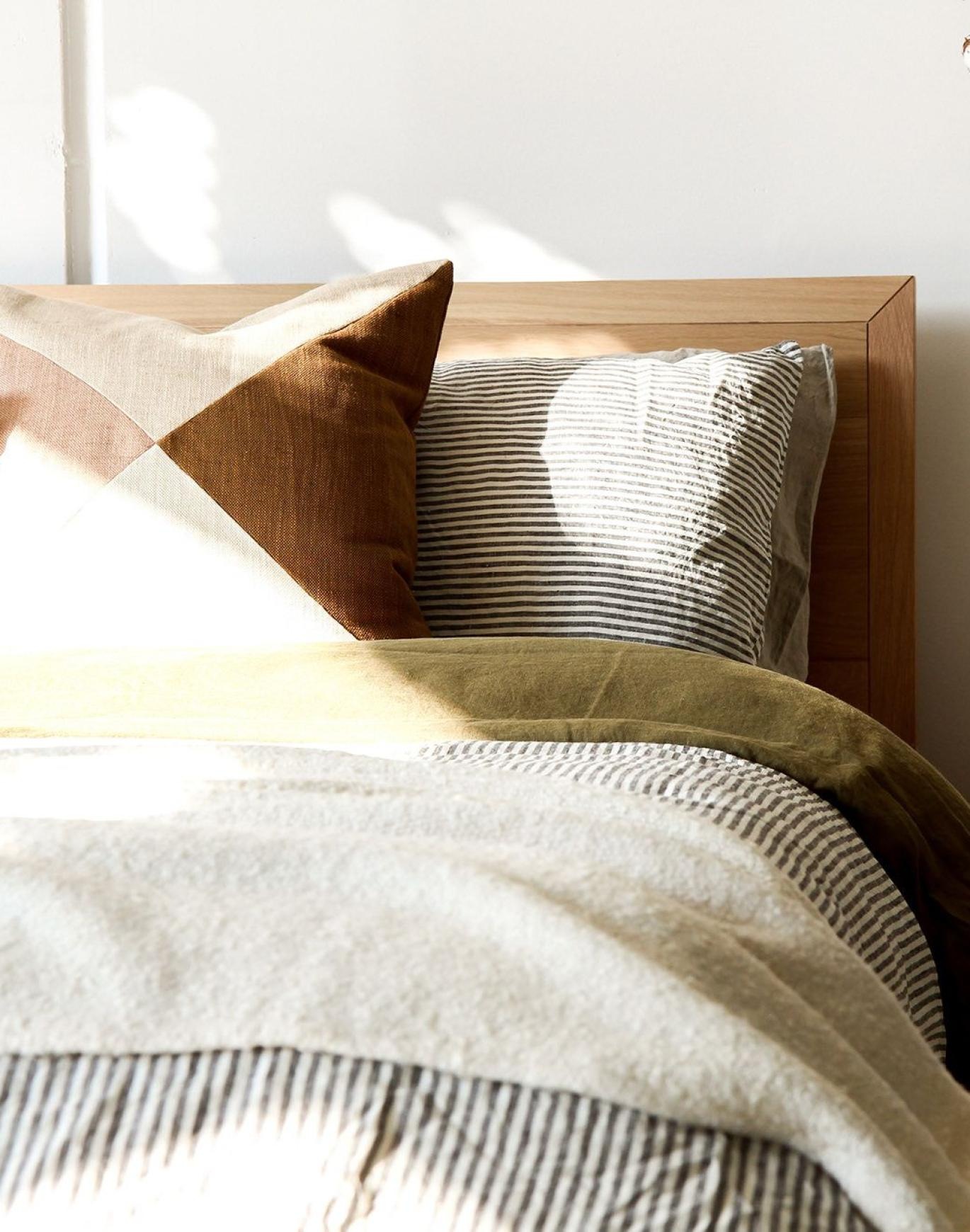 swath of sunlight shines across a well made bed and bedside table with a vase of cotton plants